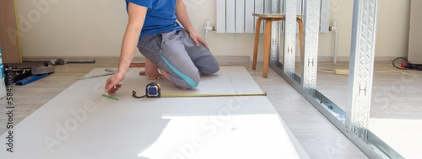 Fototapeta A man makes repairs in the room. Installing an interior wall. Pano.