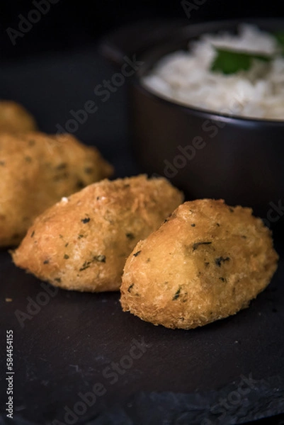 Fototapeta Bolinhos de bacalhau, very famous in Portuguese gastronomy. Fried dumpling, cod dumpling, fish, salted cod fritters, bacalao bunuelos. Codfish cake served with white rice on a dark background.