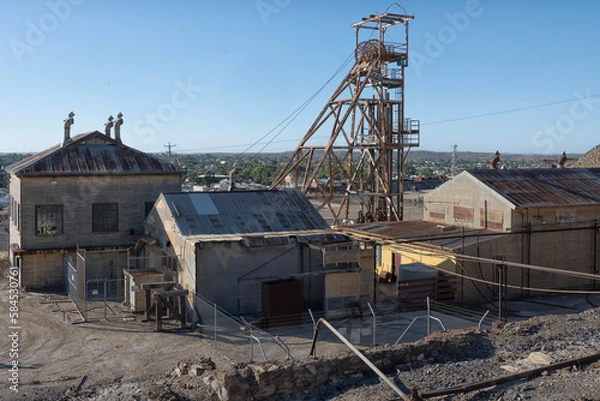 Fototapeta View of headframe and buildings at old mining site in Broken Hill, NSW, Australia with townscape in the background. This area of Broken Hill is where the mining company BHP was founded in 1885. 
