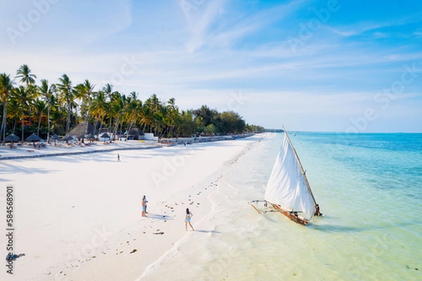 Fototapeta The natural beauty of Zanzibar's tropical coast is on full display in this aerial view, with fishing boats lining the sandy beach at sunrise. The top-down perspective showcases clear blue waters,