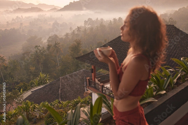 Fototapeta Woman enjoys a relaxing yoga retreat at a beautiful Bali resort with stunning views of the sunrise and Agung volcano. Travel and wellness concept.