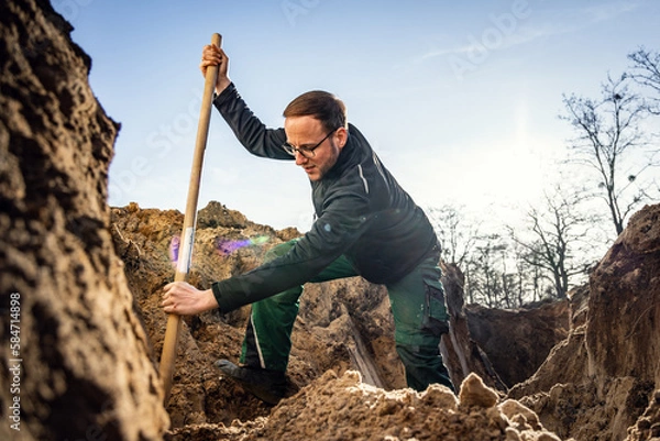 Fototapeta Worker inside a large hole digging with a shovel