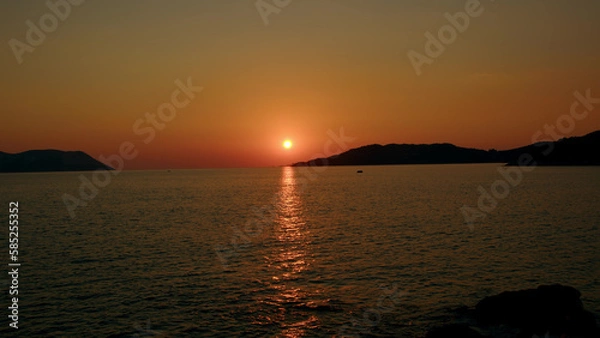 Fototapeta Fiery red sunset over sea between mountains in sea or ocean. Picturesque sunrise with sunny path on water. concept of end of career or its beginning. Natural phenomenon in morning.