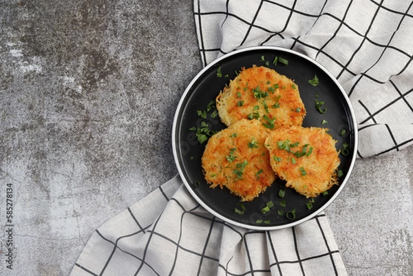Fototapeta Rustic hash browns with chives on a round plate on a dark background. Top view, flat lay