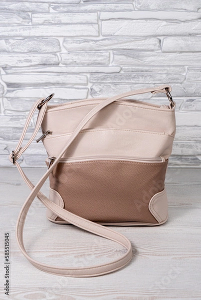 Obraz Women's beige bag with a long belt. Cross-body made of artificial leather. Gray and black background.