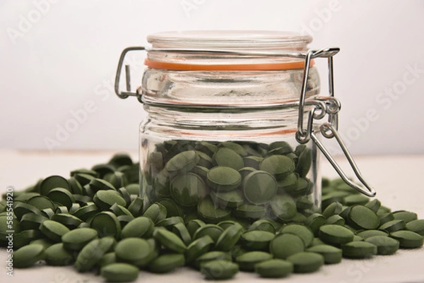 Fototapeta Green tablets of bio chlorella in a glass jar. A health-promoting dietary supplement rich in vitamins. Chlorella vulgaris.