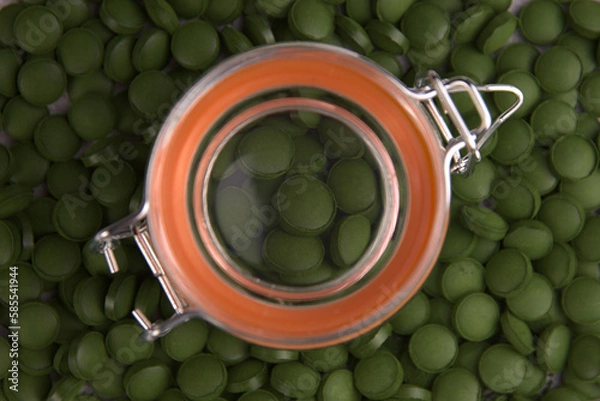Fototapeta Green tablets of bio chlorella in a glass jar. A health-promoting dietary supplement rich in vitamins. Chlorella vulgaris.