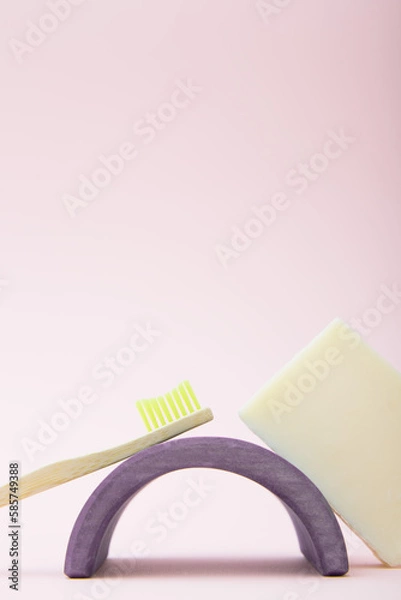 Fototapeta Composition of a bamboo toothbrush, soap and a wooden arch on a pink background. The concept of routine hygiene and personal care. Eco materials and life without plastic. Vertical photo, copy space