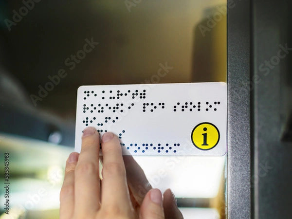 Obraz Hand of a person with blindness touches and reads Braille text plate with his hands on the door of a public transport. Close-up of a womans fingers touching the relief of points.