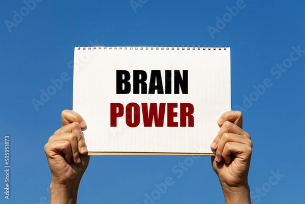 Fototapeta Brain power text on notebook paper held by 2 hands with isolated blue sky background. This message can be used as business concept about brain power.
