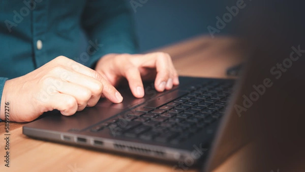 Fototapeta Close-up shot of young man working and typing on laptop computer keyboard on wooden table in cafe. Chat with AI or artificial intelligence using an artificial intelligence chatbot developed.