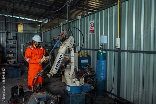 Fototapeta Male engineer holding robot controller for maintenance or repair automatic robotic machine in factory. Male technician worker working with control automatic robot arm system welding in the factory