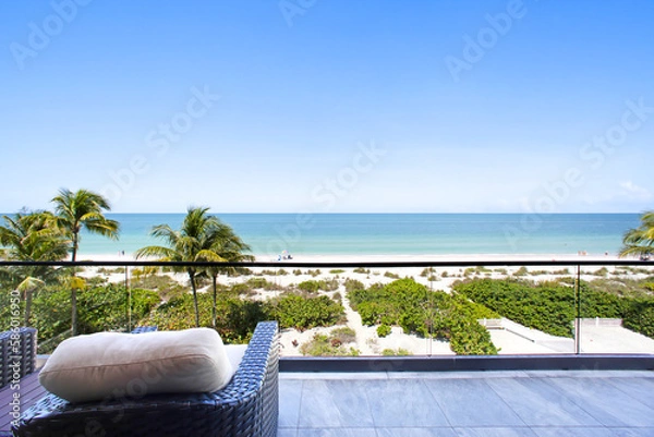 Fototapeta Beach View Balcony with Palm Trees, Sand, and Clear Blue Sky in Naples, Florida Overlooking Calm Blue Ocean Waters
