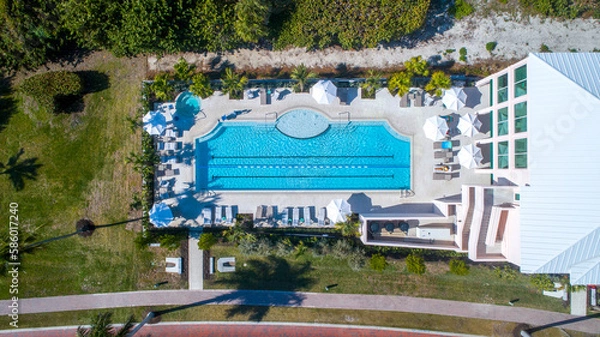 Fototapeta Aerial Drone View of Large Swimming Pool with Lush Landscaping and Umbrellas Next to a Gated Community Clubhouse in Florida