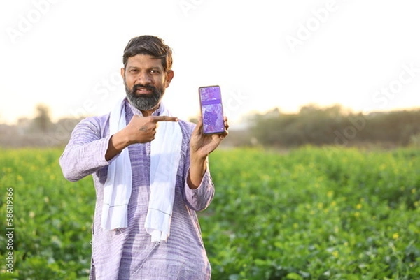 Obraz Happy rural Indian farmer pointing at the screen of his smart phone, showing his mobile phone's screen while looking at the camera .