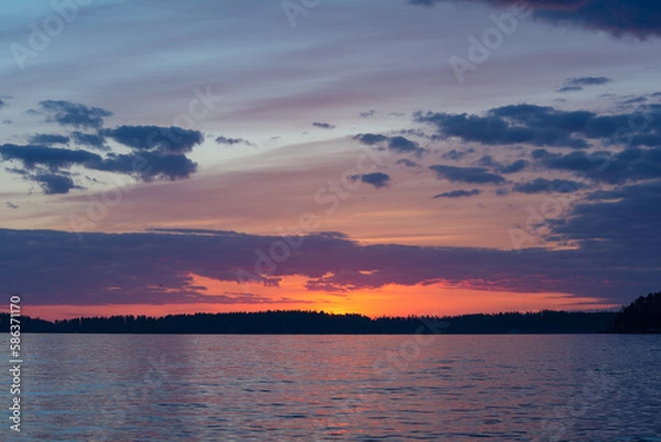 Fototapeta Purple colored clouds over a forest and a lake just after sunset