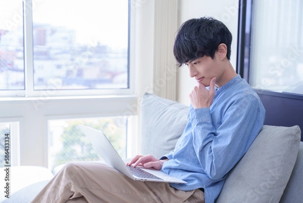 Obraz 窓辺でパソコンを見て考える男性