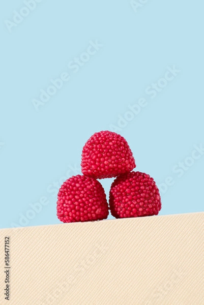 Obraz Red raspberry gummy candies on showcase, blue background. Sweet candy concept.
