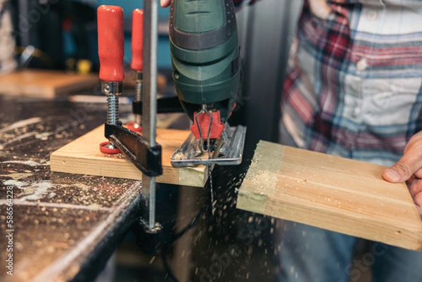 Fototapeta Woman cutting a wooden plank with an electric jigsaw in a workshop
