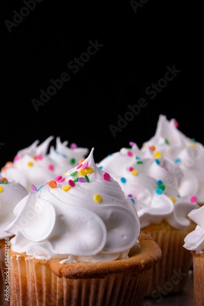 Obraz Fluffy vanilla cupcakes, with meringue and dragees on a black background.