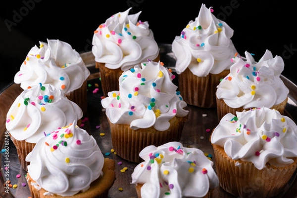 Obraz Fluffy vanilla cupcakes, with meringue and dragees on a black background.