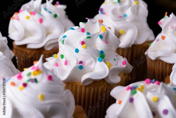 Obraz Fluffy vanilla cupcakes, with meringue and dragees on a black background.