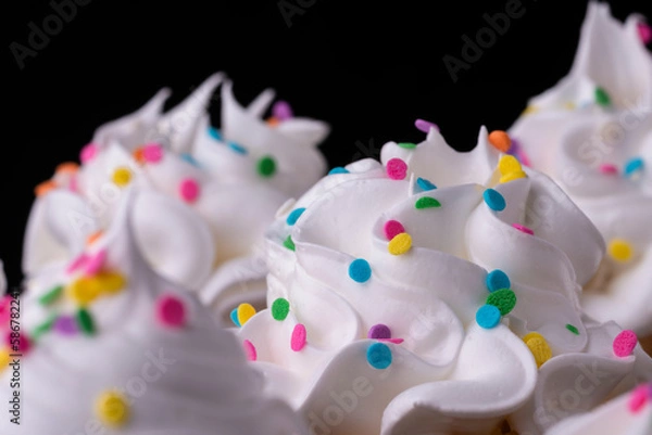 Obraz Fluffy vanilla cupcakes, with meringue and dragees on a black background.