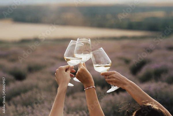Fototapeta Group of friends with white wine in hands clinking with glasses. Close-up of hands and drinks. Beautiful scenic landscape.	
