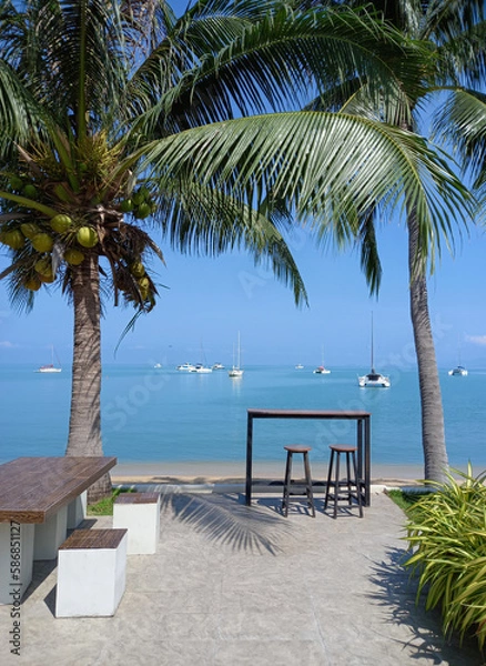 Fototapeta Table and chairs on the beach in Koh Samui, Thailand. Ocean landscape with boats as background. 
