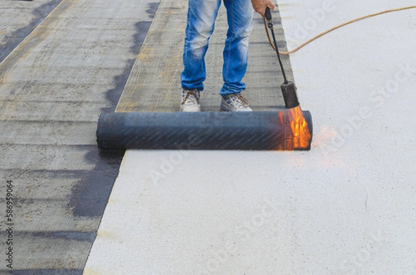 Obraz workers insulating rooftop with bitumen membrane. Waterproofing details at construction site. System details and installation on flat rooftop.