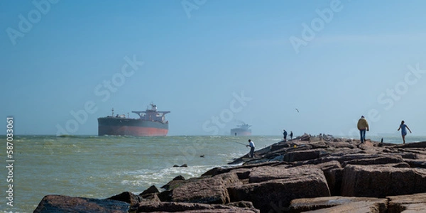 Obraz The South Jetty concrete sidewalk, with people fishing and walking, and oil tanker ships approaching from the Gulf of Mexico on the channel to Corpus Christi, Texas. 