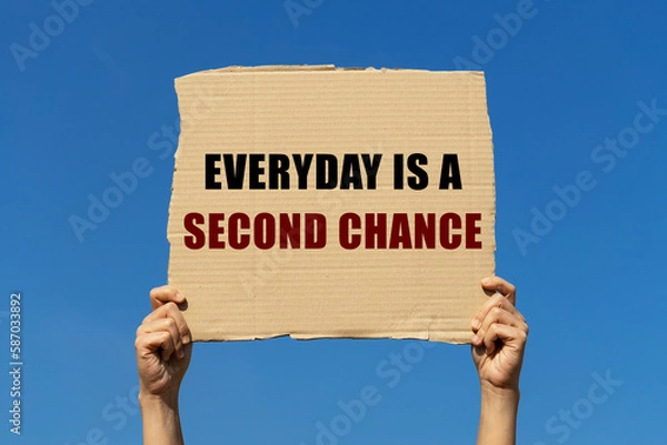 Fototapeta Everyday is a second chance text on box paper held by 2 hands with isolated blue sky background. This message board can be used as business concept about second opportunity.