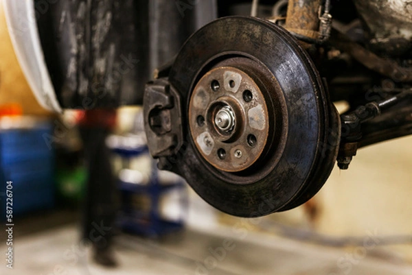 Fototapeta A close-up of the brake caliper on an old car that is lifted on an electric lift in a workshop.