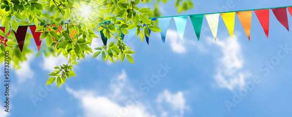 Obraz colorful pennant string decoration in green tree foliage on blue sky, summer party background template banner with copy space