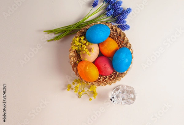Fototapeta in a small basket are multi-colored painted eggs. flowers lie nearby. Top view