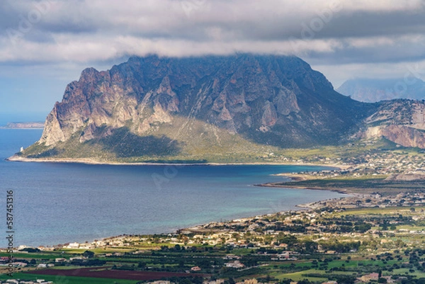 Fototapeta A beautiful seaside mountain covered with a dark rainy cloud below with a town.