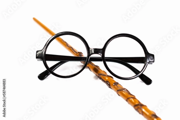 Fototapeta Round black eyeglasses and brown magic wand isolated on white background. Harry Potter style circle glasses and wand. Wizard costume accessories. 
