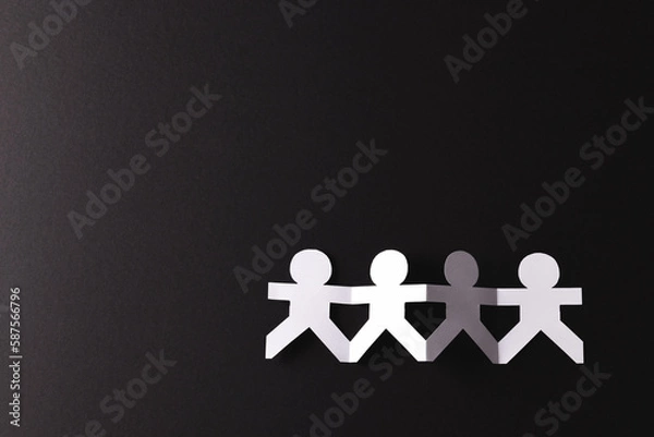 Fototapeta Close up of four paper cut out people figures holding hands with copy space on black background