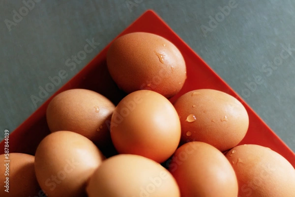 Fototapeta Eggs stacked in the corner of a red tray on silver aluminum surface in top view.