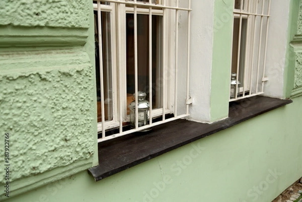 Fototapeta Lanterns for a heating candle in a window opening with a metal grill, viewed from the street