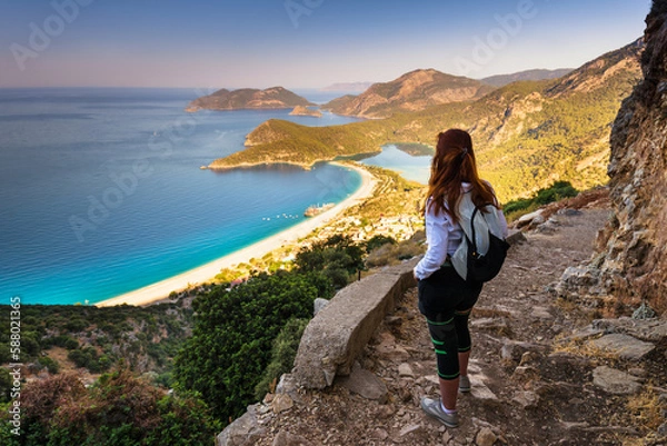 Fototapeta Hiking on Lycian way trail. Young girl with backpack enjoy view of Oludeniz beach and Blue Lagoon from Lycian way trail. Mediterranean coast. Fethiye. Turkey.