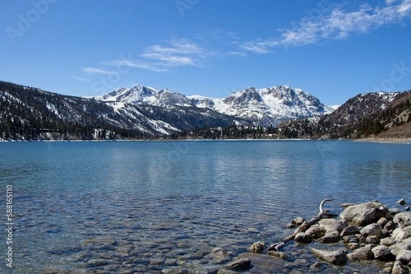 Fototapeta Snow tops the Sierra Nevada Mountains from the crystal clear waters of June Lake, which sits at the bottom of the mountain range's steep eastern escarpment