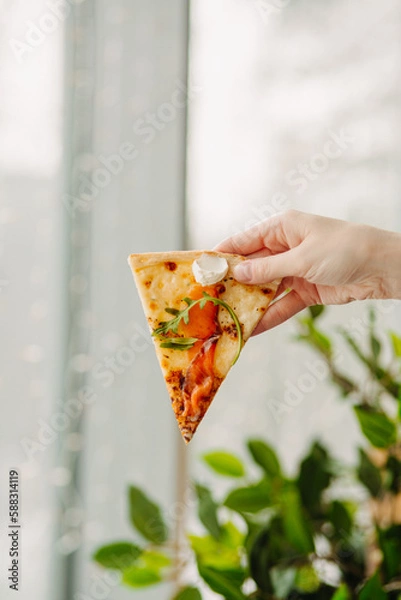 Fototapeta A piece of pizza in his hand, against the backdrop of the restaurant, Side view of the pizza. The concept of Italian cuisine, street food, fast food, fast food. Banner