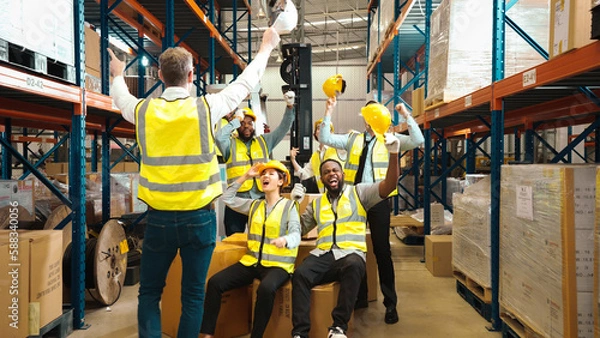 Obraz Multiracial warehouse workers in safety wear are stacking hands and cheering to celebrate after finishing a job in warehouse. Male and female logistic employees are enjoying the achievement together.