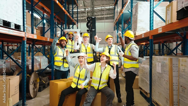 Obraz Multiracial warehouse workers in safety wear are dancing to relax after working hard on shipping goods. Male and female logistic employees are spending time together to celebrate the success of jobs.