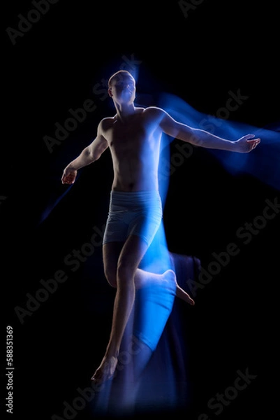 Obraz Portrait of young guy wearing underwear jumping in motion over dark background. Futuristic man from future. Mixed neon light
