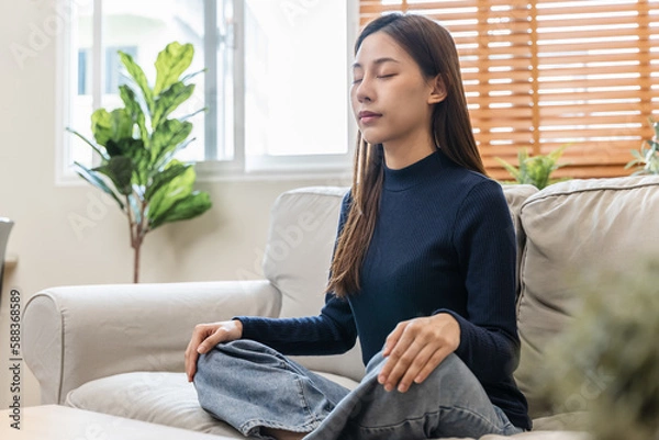 Fototapeta well being meditation. Asian women sit in the living room and practice mindfulness by focusing on breath concentrate.