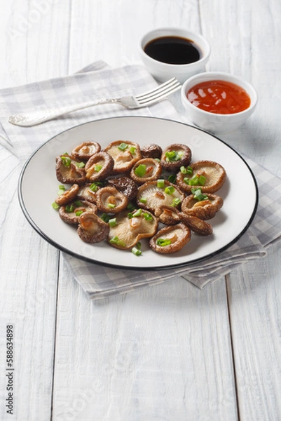 Fototapeta Fried shiitake mushrooms close-up on a plate served with chili and soy sauces on a wooden table. Vertical