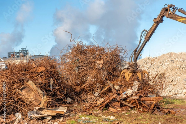 Obraz A grapple truck loads scrap industrial metal for recycling. Manipulator with a hydraulic magnetic crab against the sky. Crane garbage truck loading of industrial waste.