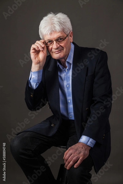 Fototapeta Portrait of an elderly man with glasses and a dark business suit on a dark background. 